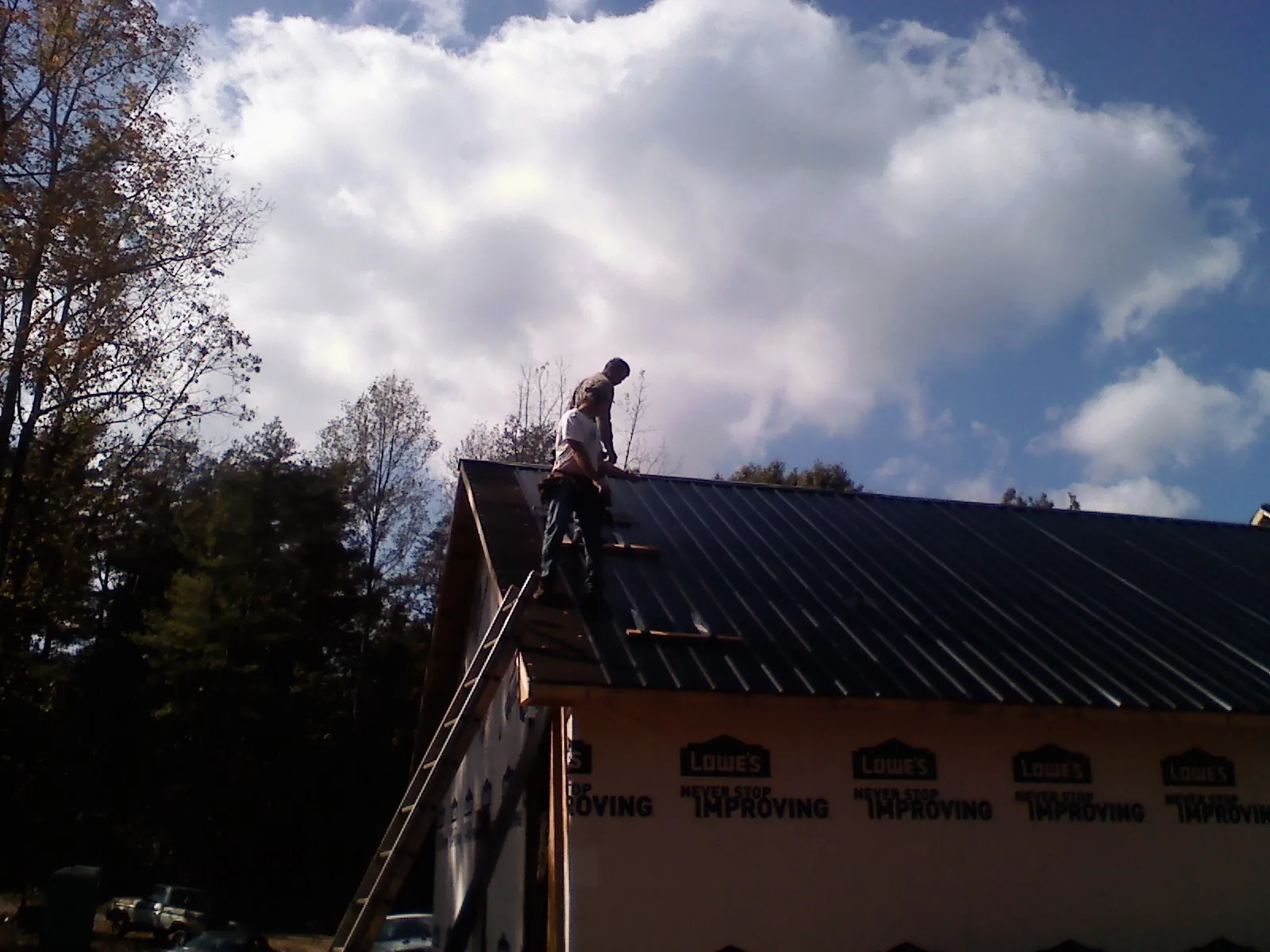 Roofer fastening dark metal panels high against a cloudy sky, from a Roof Inspection job in San Antonio